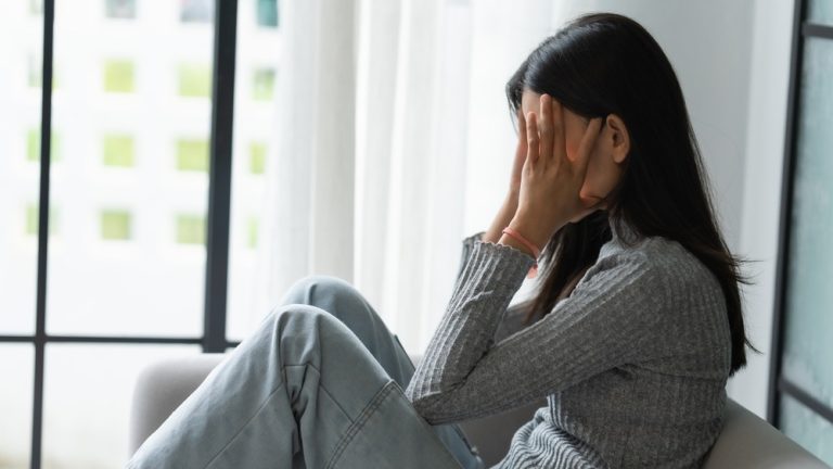 坐在窗邊掩面沉思的女性，示意備孕與不孕治療中的壓力困擾